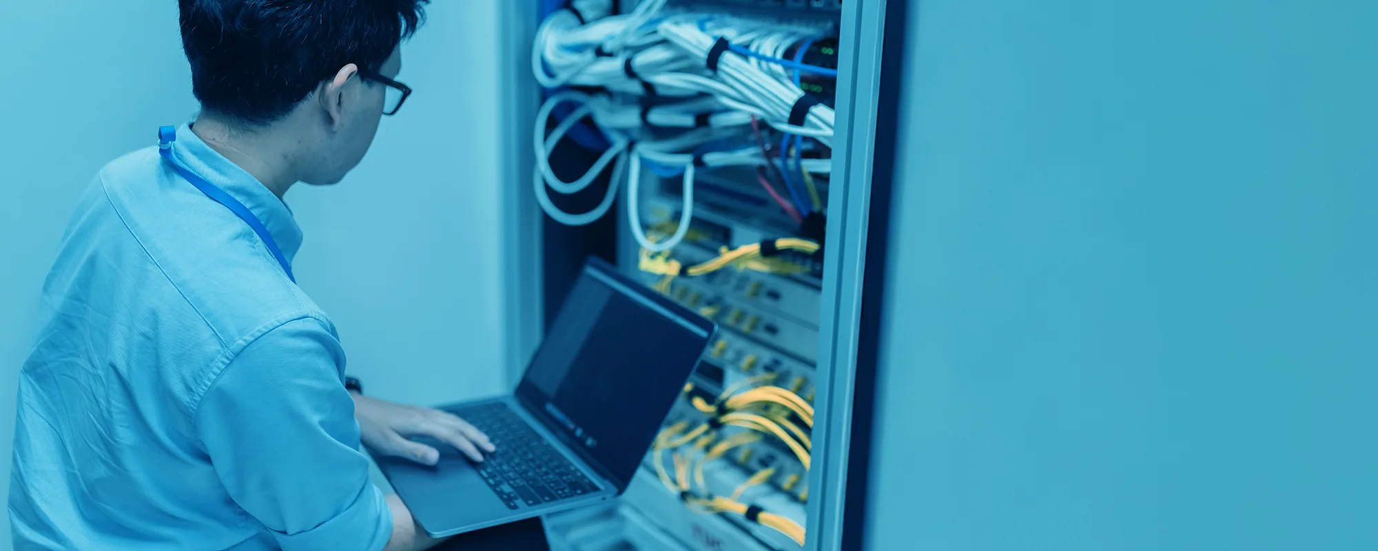 Ingeniero de soporte trabajando con una laptop frente a un rack de comunicaciones